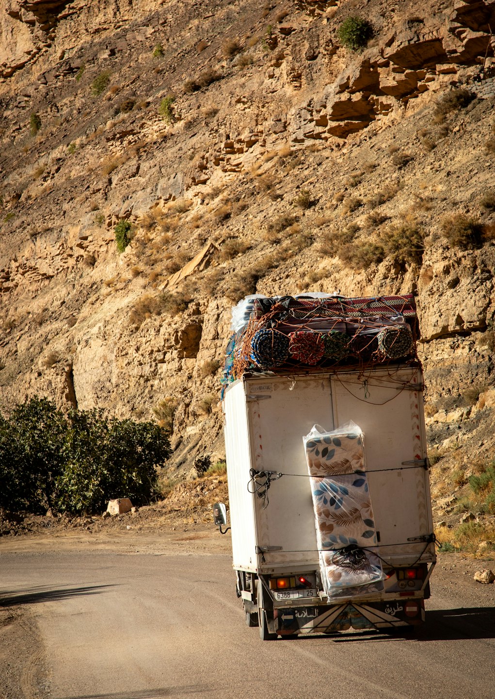 A loaded delivery truck drives away on a mountain road.