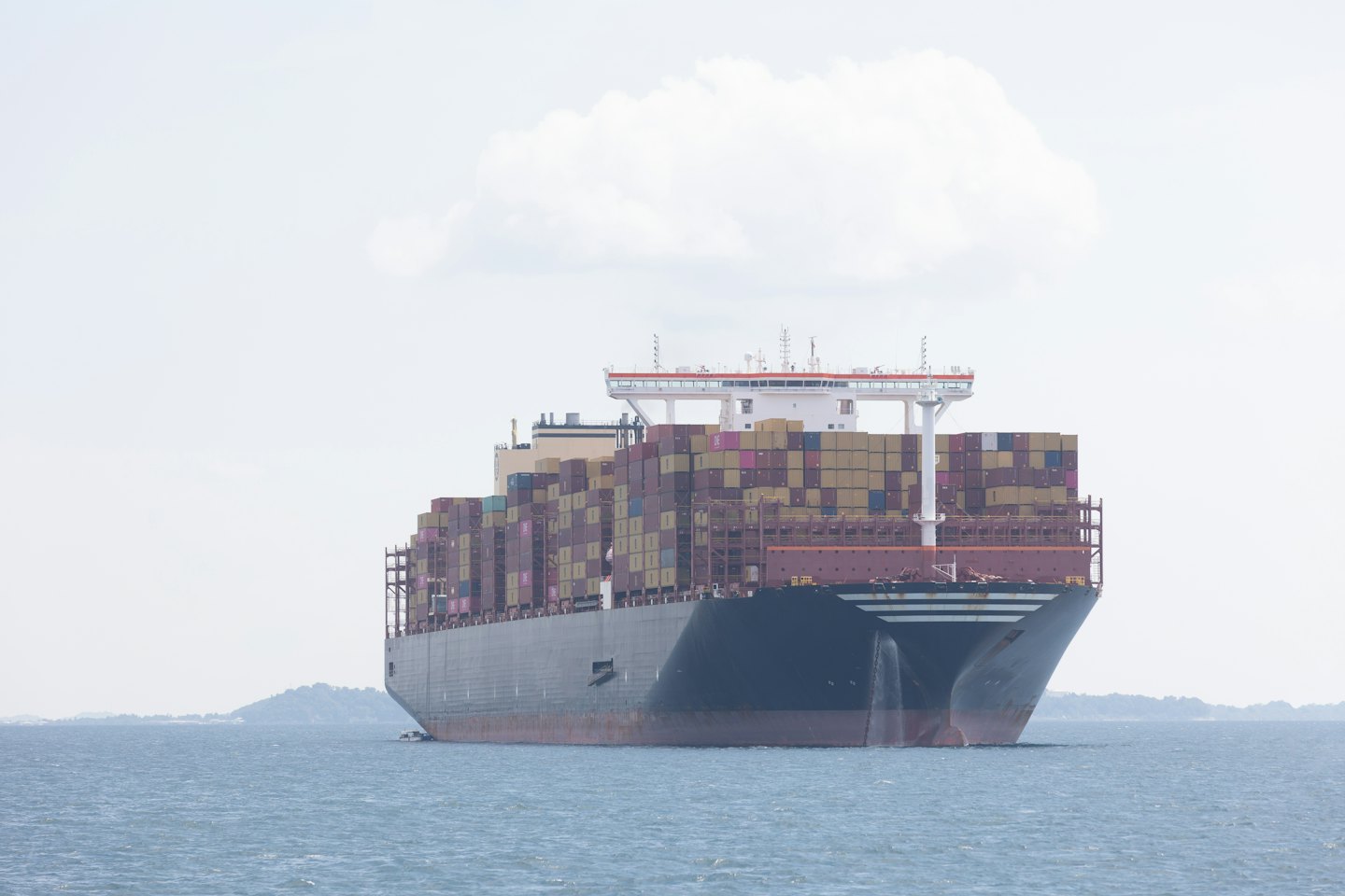 A large container ship loaded with cargo sails across the ocean.