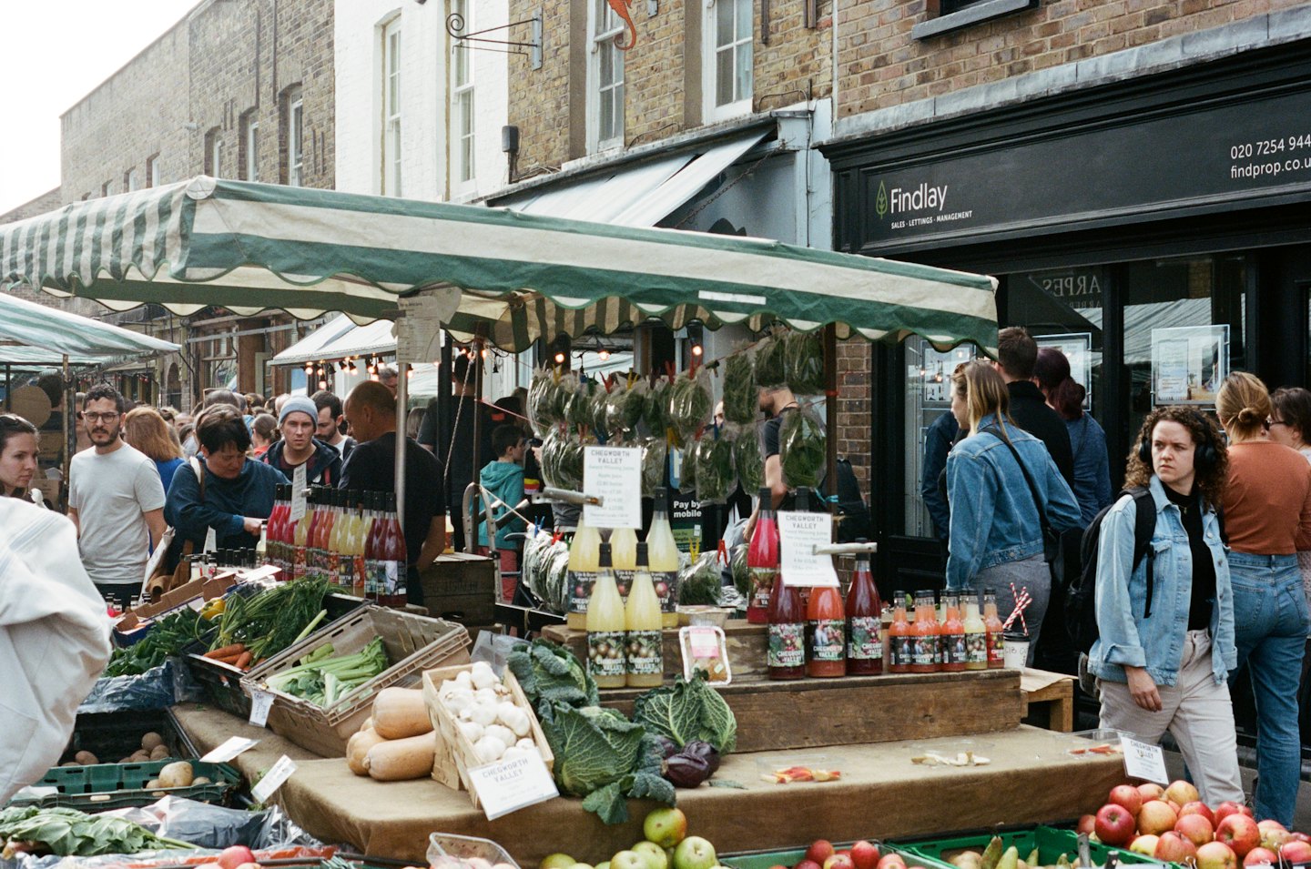 People shop for fresh produce and bottled goods at a busy outdoor market.